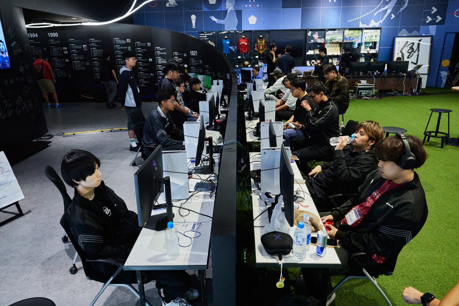 PS5が並んだ競技エリア。日本サッカーの歴史を展示した壁の前で選手たちが対戦している