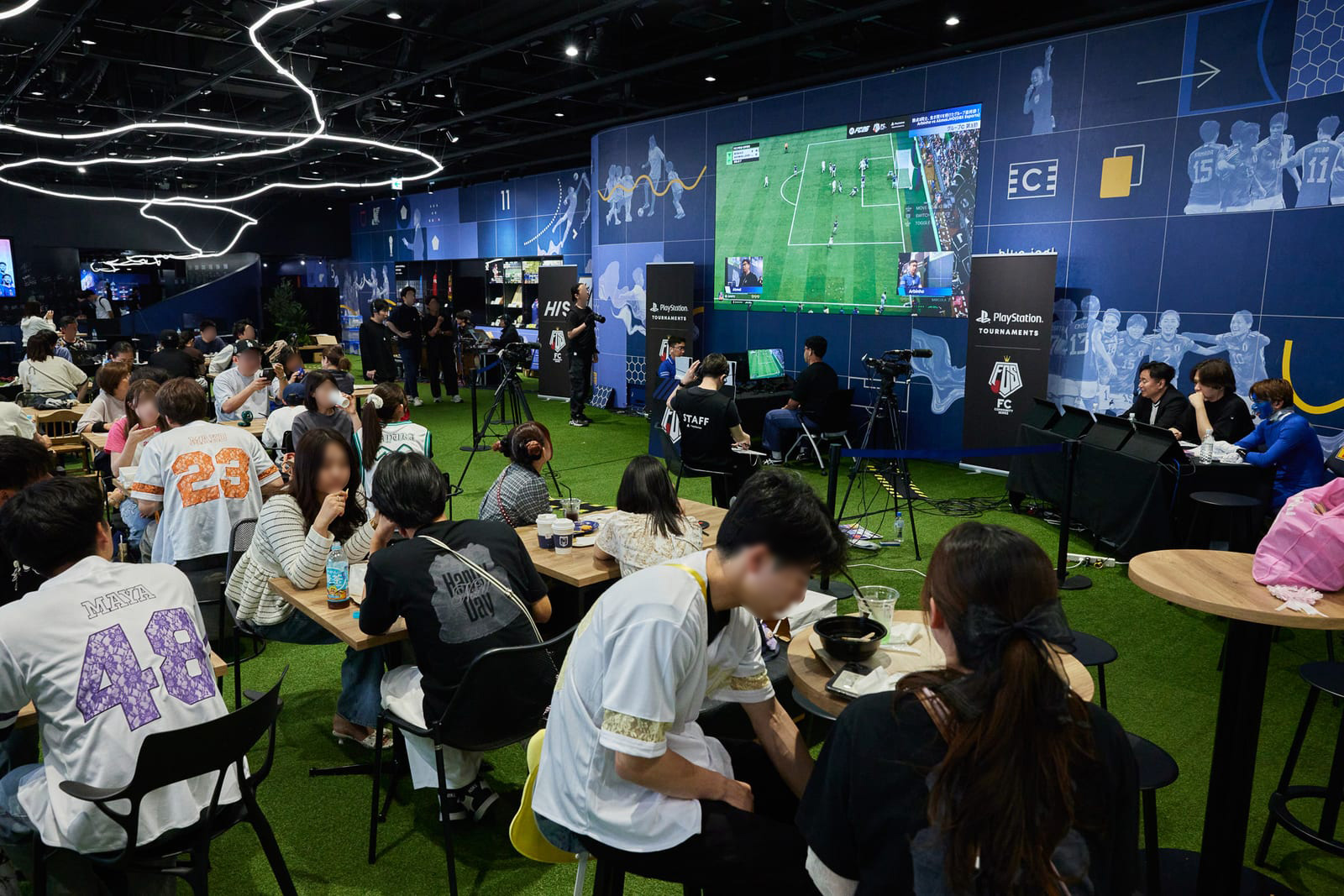 大型ビジョンに試合が映し出され、その前のテーブルで来場者が観戦している
